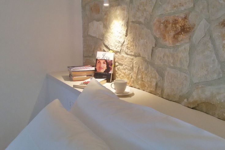 Eine gemütliche Zimmerecke mit Büchern auf einem Regal, einer Tasse Kaffee auf dem Tisch und einer Steinmauer.