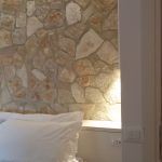 Schlafzimmer mit Steinwand und einfachem weißen Bett.