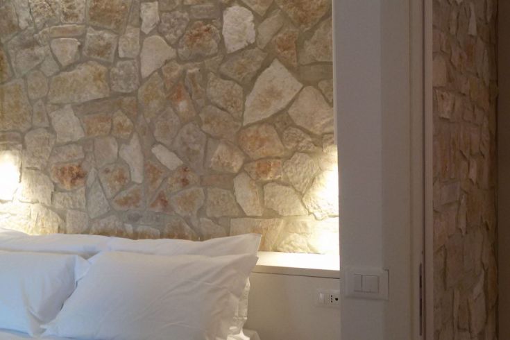 Innenansicht eines Zimmers mit einer Steinwand und weißen Betten.