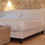 Ein einfaches weißes Bett in einem gemütlichen Zimmer mit Steinwänden.