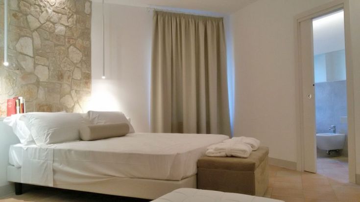 Ein Zimmer im Landhausstil mit einem Doppelbett, dekoriert mit natürlichen Materialien und Steindetails. Barrierefreies Bad im Hintergrund.