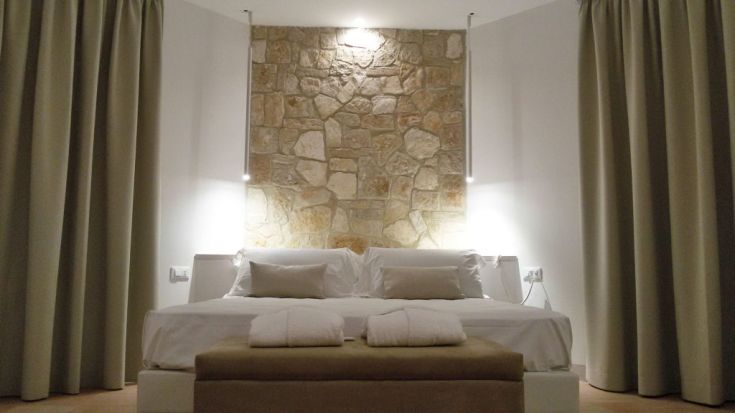 Moderne Schlafzimmergestaltung mit Steinwand, bequemen Betten und leichten Vorhängen.
