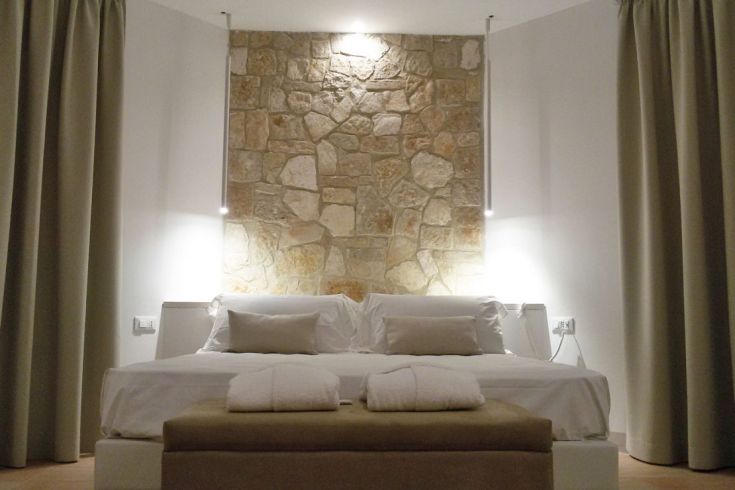 Ein schlichtes Zimmer mit einer Steinwand und weißen Bettwäsche, sanft beleuchtet.