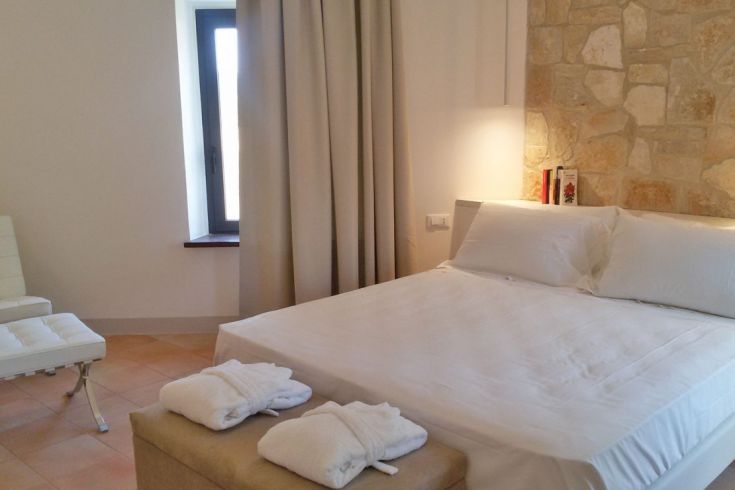 Ein minimalistisches Schlafzimmer mit einem Doppelbett, schlichten Möbeln und Steindetails.