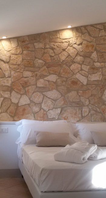 Einfache Zimmer mit einem weißen Bett und Steinwänden, sanft beleuchtet.