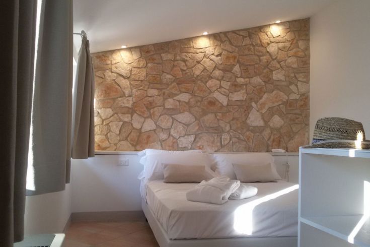 Innenraum eines Zimmers mit Steinwänden, einem weißen Bett und sanfter, zarter Beleuchtung.