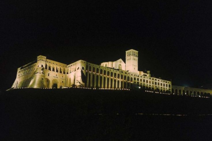 Die Basilika San Francesco in Assisi, ihre Fassade gut sichtbar und im Dunkeln der Nacht beleuchtet.