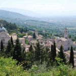 Szene eines alten Dorfes, umgeben von Grün, mit Kirchen und Hügeln in der Ferne.