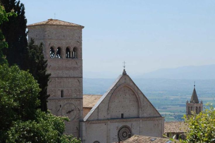 Eine Szene mit historischen Kirchen mit Glockentürmen, umgeben von der grünen Landschaft Umbriens.