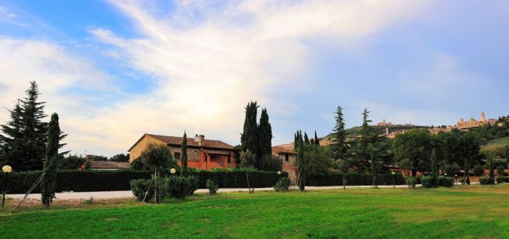 Eine Villa, umgeben von Gärten und Bäumen, unter einem klaren Himmel.