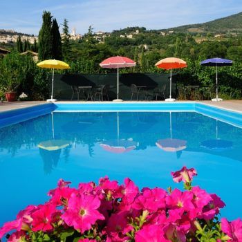 Ein klarer Pool, umgeben von Sonnenschirmen und rosa Blumen, eingebettet in eine natürliche Umgebung.