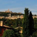 Eine hügelige Landschaft mit grünen Bäumen und einem alten Dorf in der Ferne.