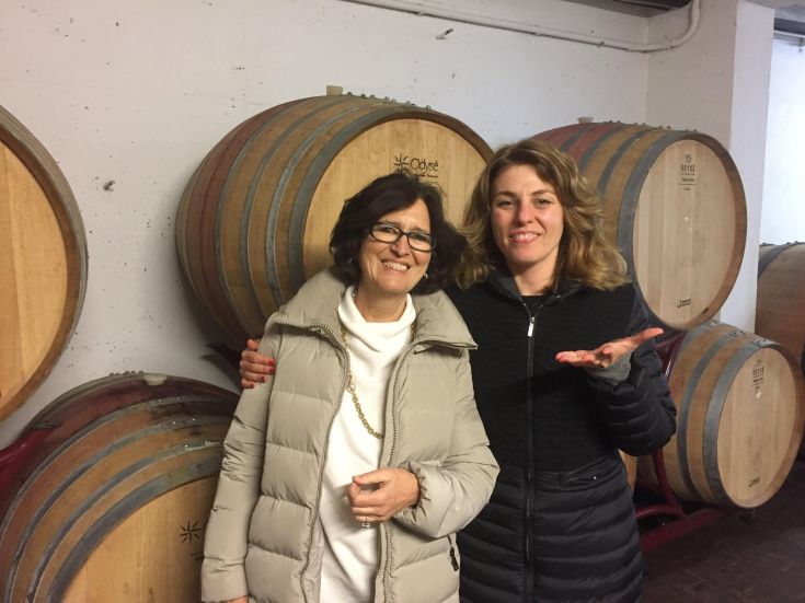 Zwei lächelnde Frauen vor Holzfässern in der einfachen Atmosphäre eines Weinkellers.