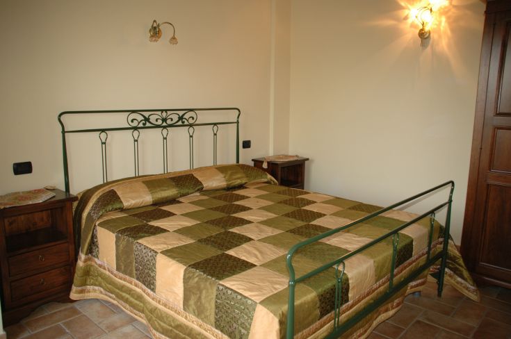 Camera semplice con letto matrimoniale, decorazioni in tonalità verdi e beige che creano un'atmosfera rilassante.