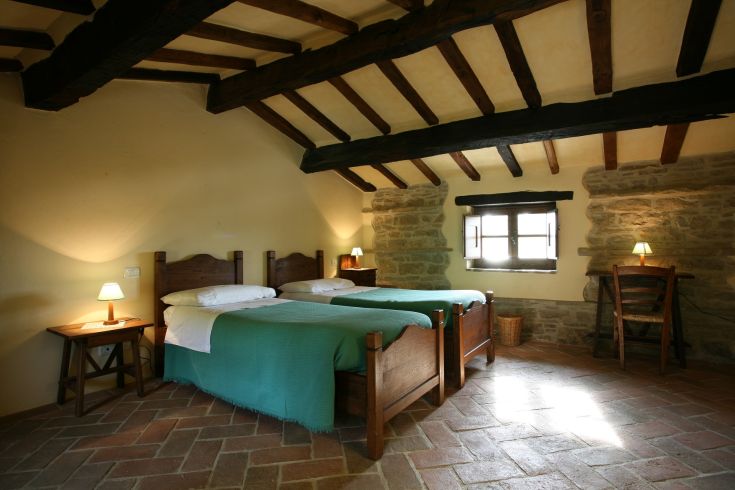 Camera rustica con due letti singoli, illuminazione calda e arredi semplici per un'atmosfera rilassante.