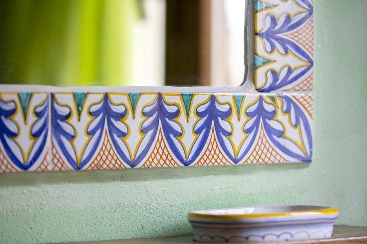 Specchio con cornice in ceramica colorata, che riflette il paesaggio naturale circostante.