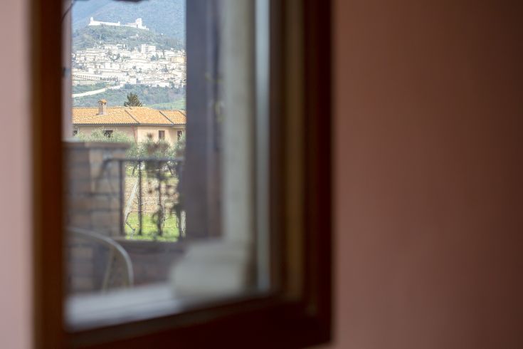 Scena di Assisi osservata da una finestra, che evidenzia il paesaggio tipico della campagna umbra.