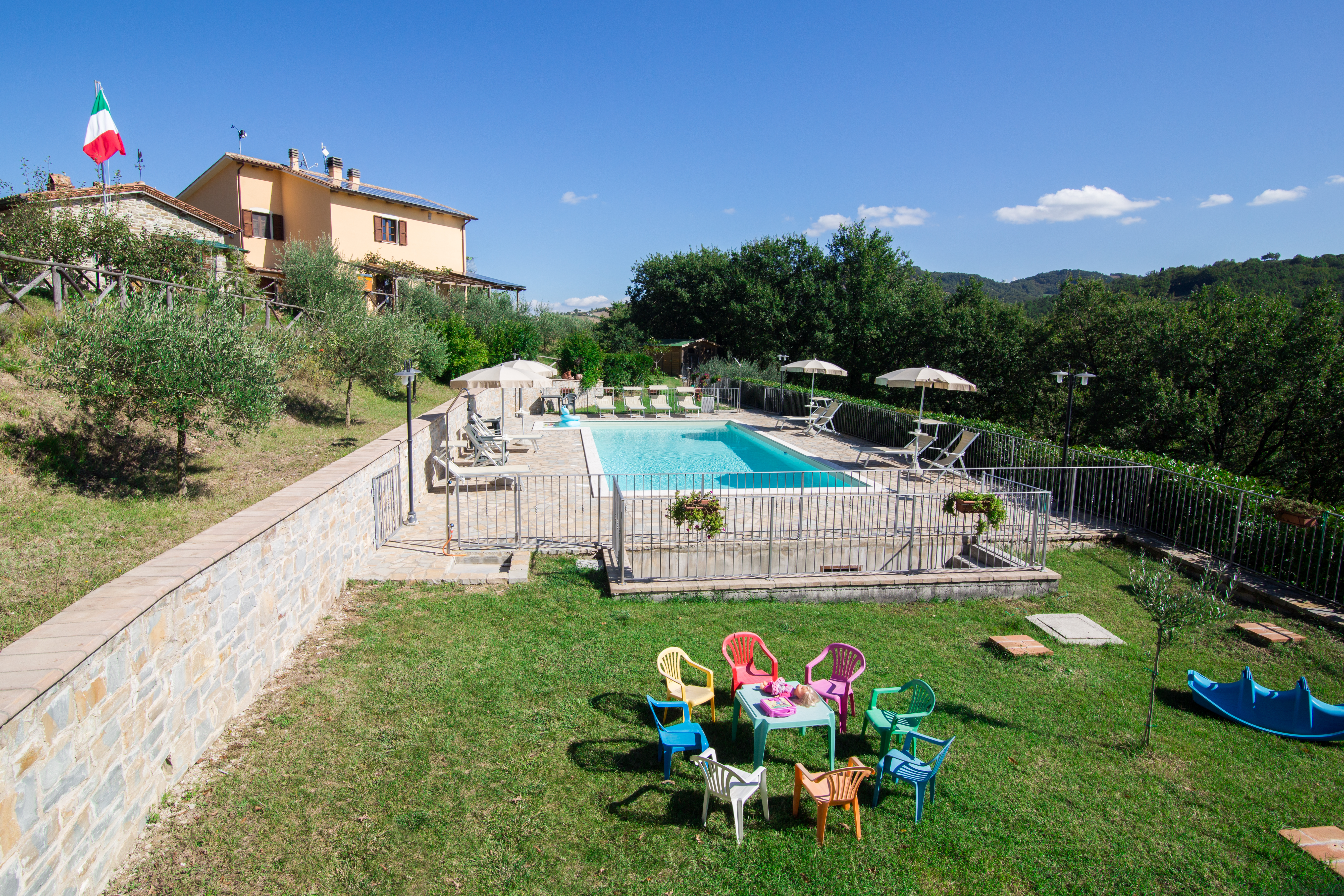 Struttura agrituristica con piscina circondata da aree verdi, adatta per momenti di relax e attività per bambini.