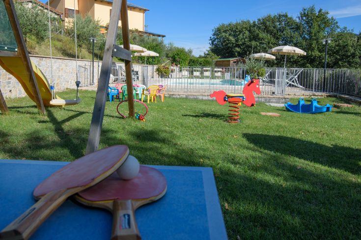 Outdoor-Spielbereich für Kinder mit Spielen und einem kleinen Pool, umgeben von Grün.