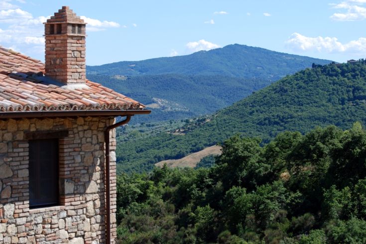 A view of the Umbrian hills with a rustic farmhouse in the foreground and rolling hills in the background.