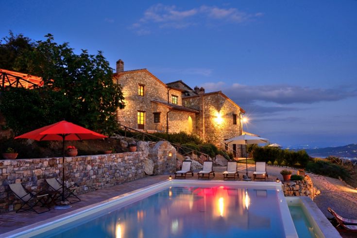 A stone villa with a pool, surrounded by nature and illuminated by the setting sun.