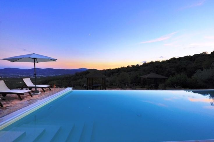 Infinity pool surrounded by hills as the sun sets on the horizon.