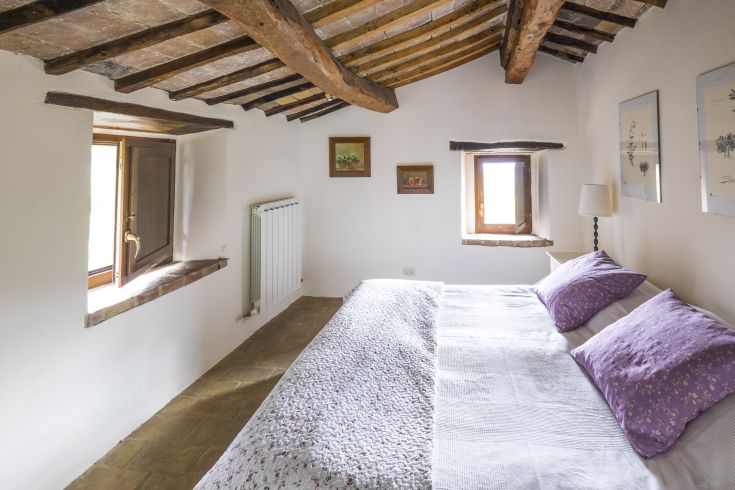 Simple room with a double bed and windows allowing natural light to fill the space.