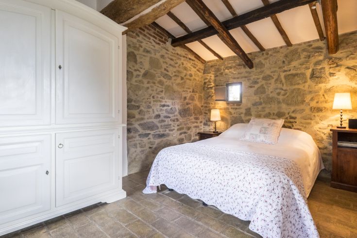 A bedroom featuring a double bed, light wardrobe, and stone walls, creating a simple and relaxed atmosphere.
