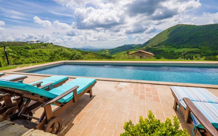 A swimming pool surrounded by green areas and distant hills.