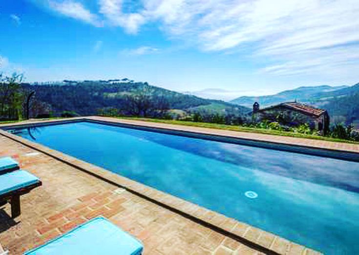A swimming pool surrounded by trees and meadows in Umbria, overlooking gentle surrounding hills.