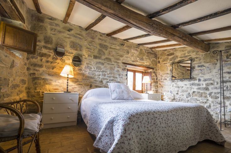 Bedroom with a simple design, featuring stone walls and wooden beams, well-furnished and bright.