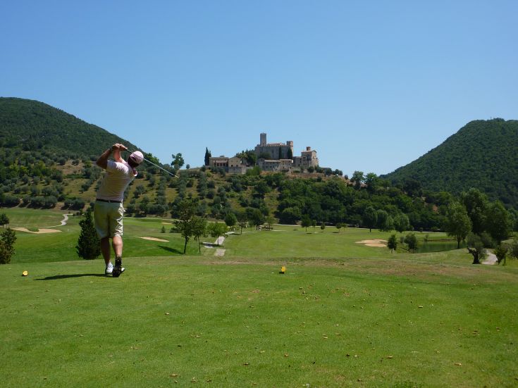A golfer readies to hit the ball, with a building faintly visible in the background.