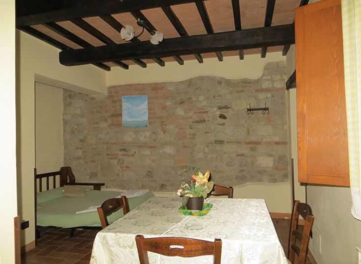 Interior of a rustic agriturismo featuring a stone wall, a rustic table, and a sofa bed.