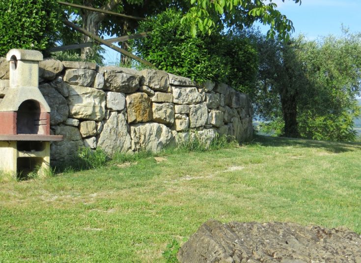 A garden with a barbecue surrounded by a stone wall, exuding the serene atmosphere typical of Umbria.