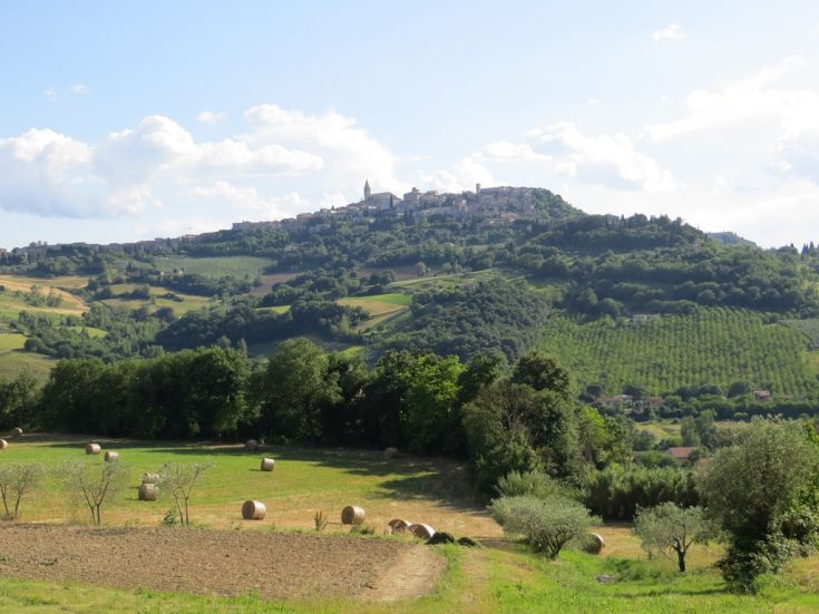 Hilly landscape with vast fields and farms, a small historic village visible in the distance.