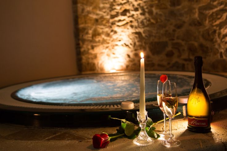 Un angolo tranquillo con una vasca idromassaggio, alcune bottiglie di champagne, rose e un'illuminazione delicata.