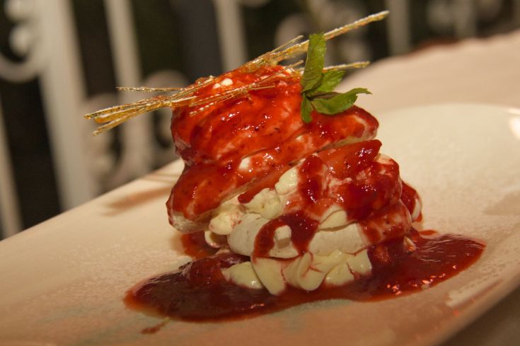 Dessert caratterizzato da panna, fragole fresche e una salsa rossa. Presentato con dettagli decorativi.