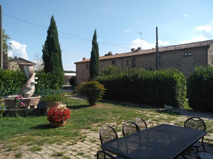 Eine malerische Agriturismo-Landschaft mit einem Garten, Pflanzen und einem Tisch im Freien neben einem dekorativen Brunnen.
