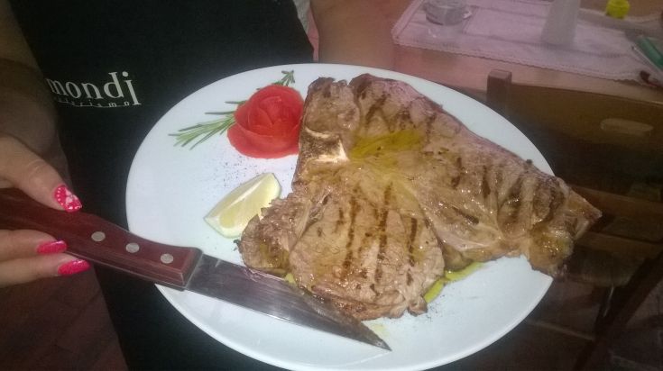 Ein gegrilltes Steak, serviert mit einer Zitronenscheibe, frischen Tomaten und einem Rosmarinzweig.