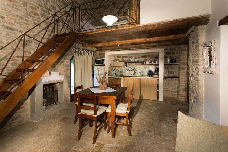 Cozy apartment interior featuring stone and wood details, a dining table, and a wooden staircase.