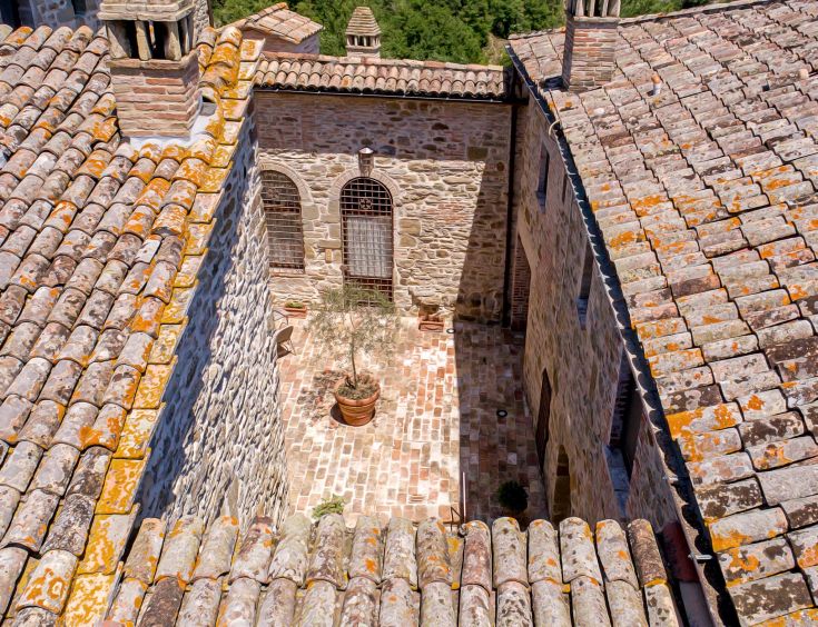 View of an inner courtyard of an ancient convent, featuring tiled roofs and a pot with plants.