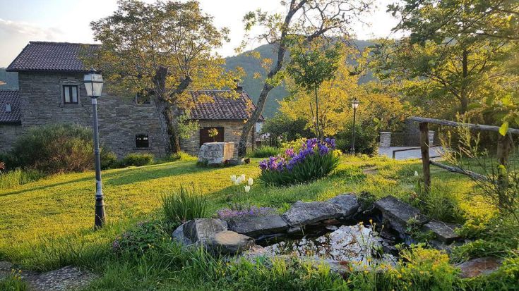 Un agriturismo circondato da un giardino verde e un lago, immerso nella natura circostante.