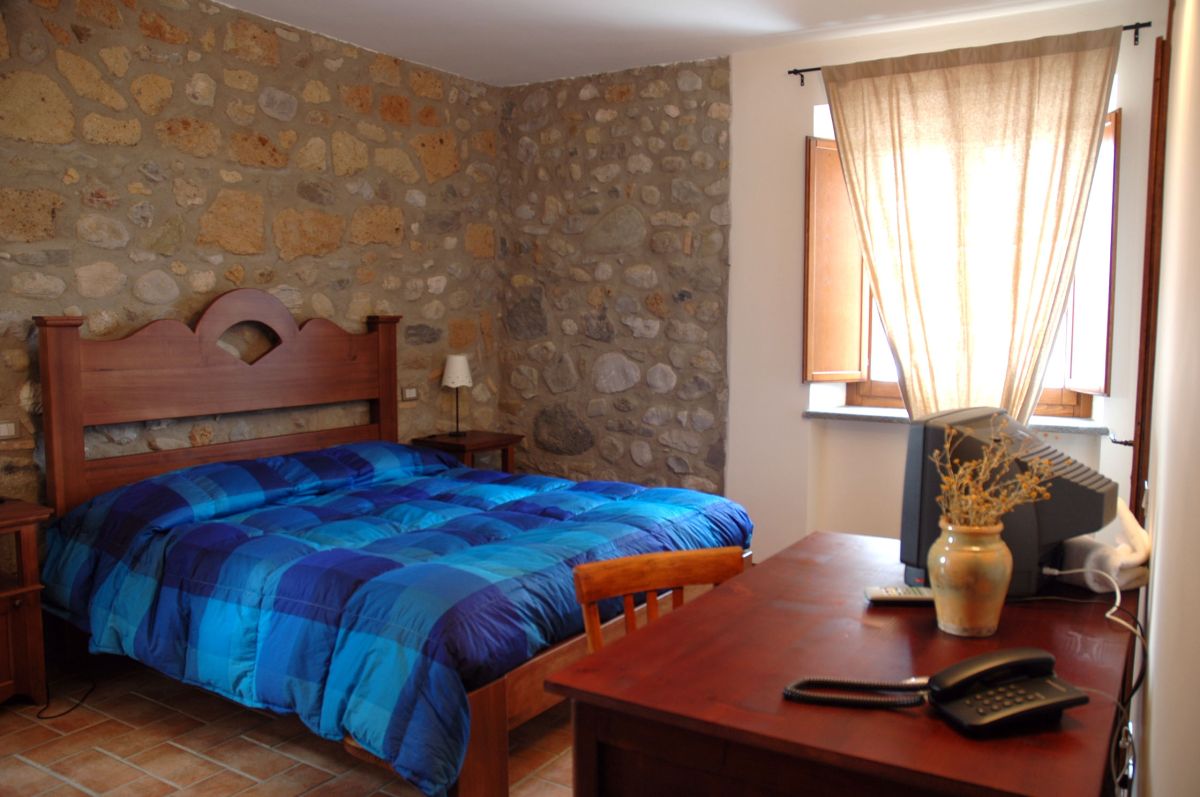 Einfaches Zimmer mit Steinwänden und einem blauen Bett, ideal für einen ruhigen Aufenthalt.
