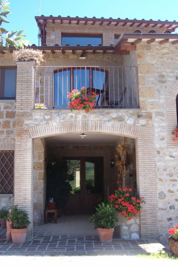 Steinbauernhaus, umgeben von Natur und Blumen, mit Tuff-Detaills in seinen Wänden.