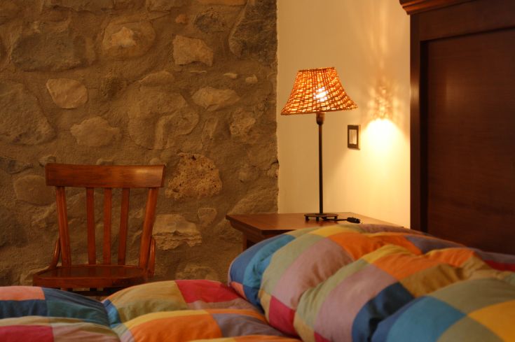 Intimer Raum mit einem lebhaften Bett, einer einfachen Lampe und einer sichtbaren Steinwand.