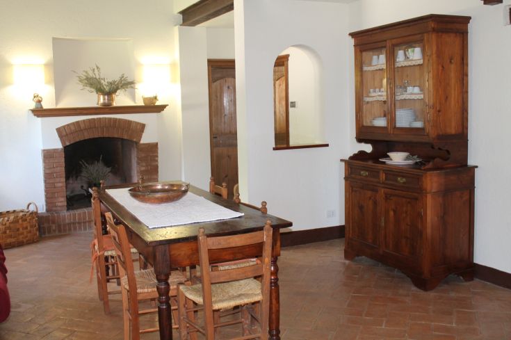 Intérieur de cuisine accueillant avec une table en bois, une cheminée et des étagères. Un espace rustique chaleureux.