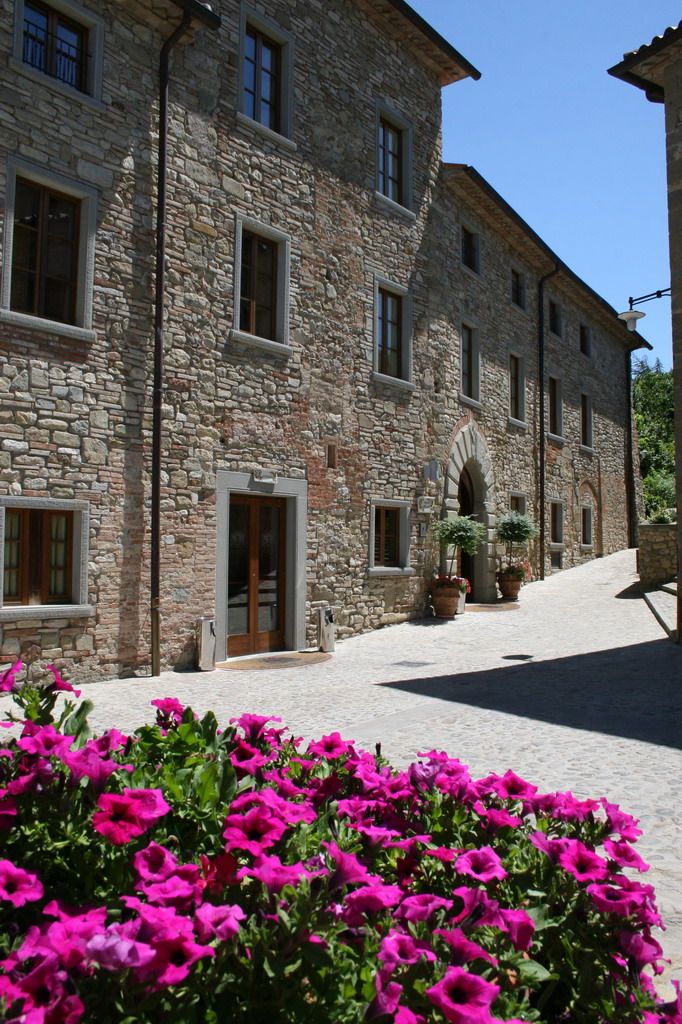 Detail eines typischen umbrischen Dorfes mit rosa Blumen im Vordergrund und historischen Steinbauten.