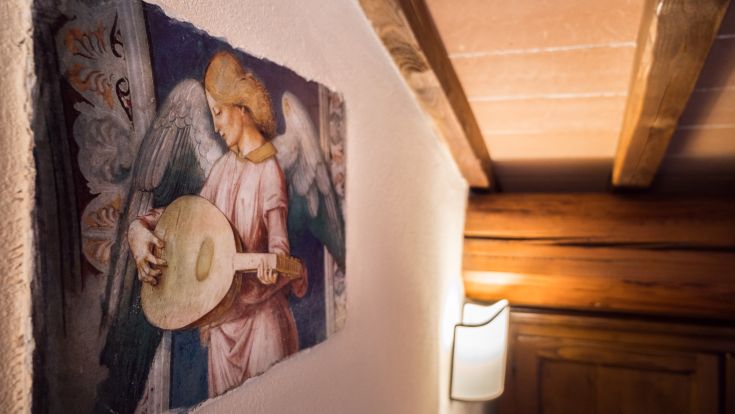 Ein Fresko, das einen Engel zeigt, der eine Laute spielt, umrahmt von dezenten historischen Elementen.