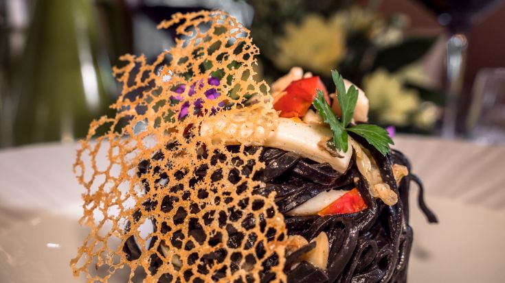 Schwarzes Pastagericht mit frischen Zutaten und einer knusprigen Waffel als Beilage.