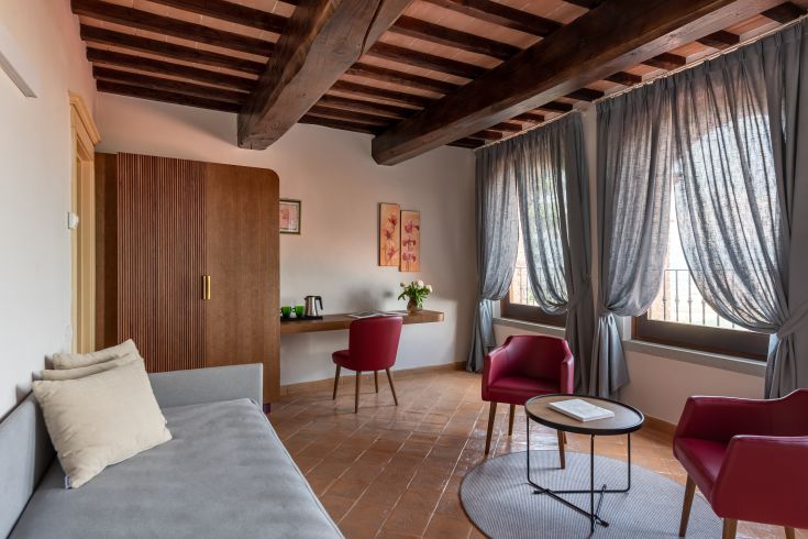 Ein helles und geräumiges Wohnzimmer mit schlichten Möbeln und großen Fenstern, die natürliches Licht hereinlassen.